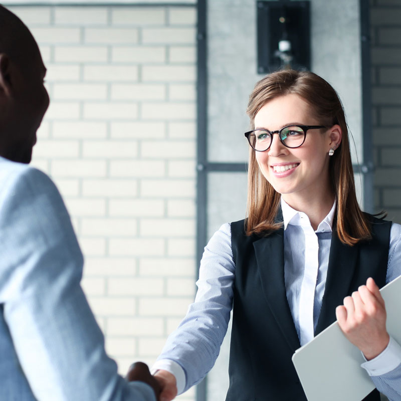 An HR coordinator exchanges a smiling handshake to a new employee.